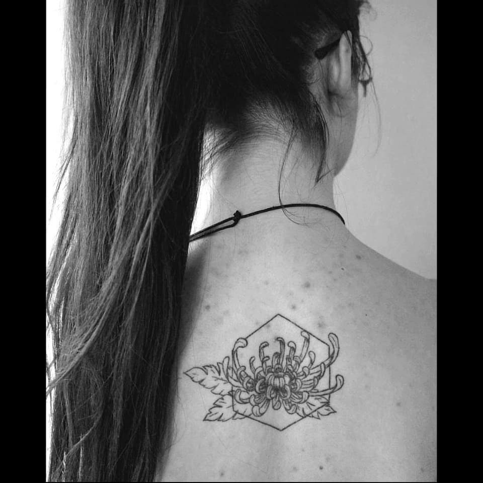 Woman with a geometric flower tattoo in a hexagon design on her upper back, featuring leaves