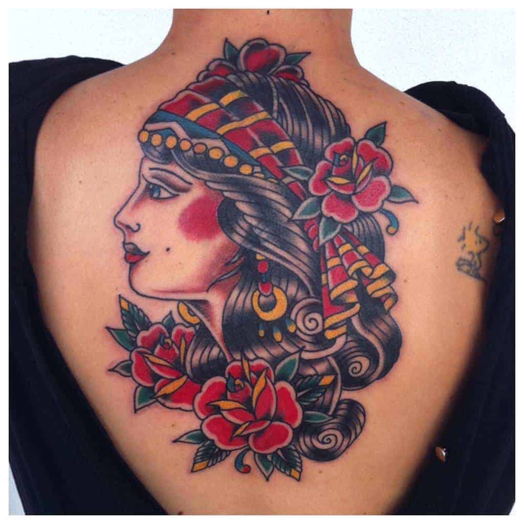 Traditional-style back tattoo of a gypsy woman with vibrant roses, gold jewelry, and a patterned headscarf