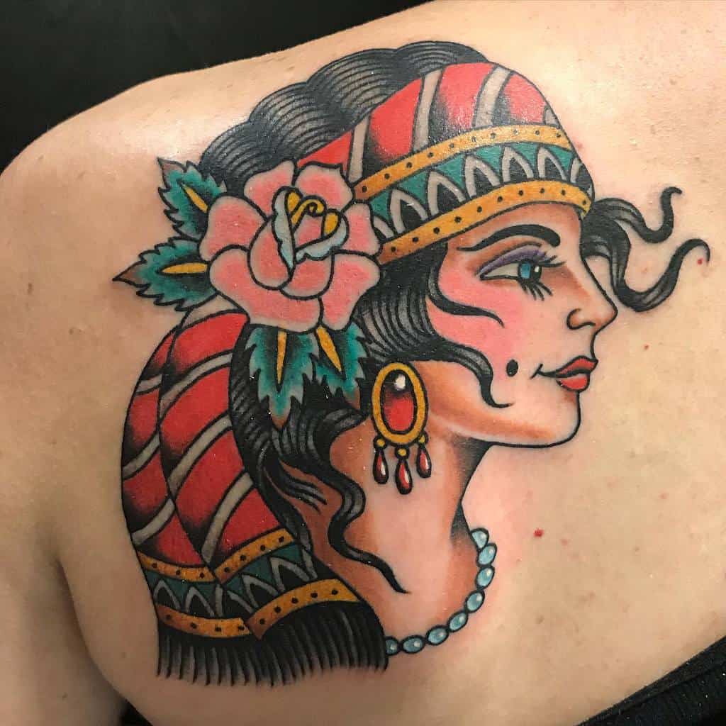 Tattoo of a gypsy woman with a headscarf, rose, and necklace on a person's shoulder