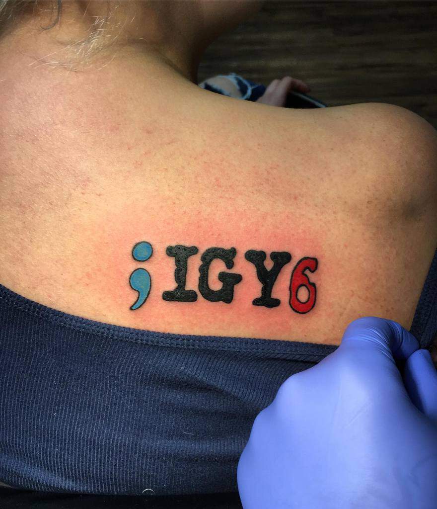 Upper back tattoo featuring ';IGY6' with a blue semicolon and red 6, symbolizing support and awareness for mental health