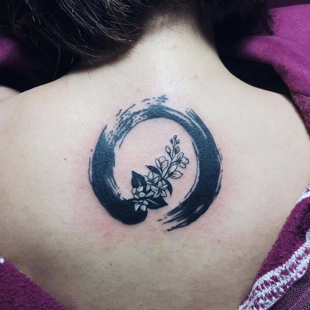Black circular brushstroke tattoo with Jasmine flower in the center on an upper back