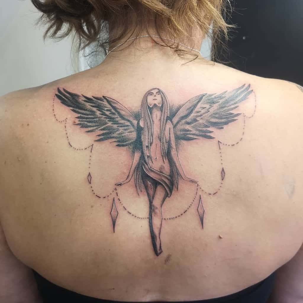 Tattoo of an angel with wings and a draped dress, surrounded by dotted lines and diamond shapes