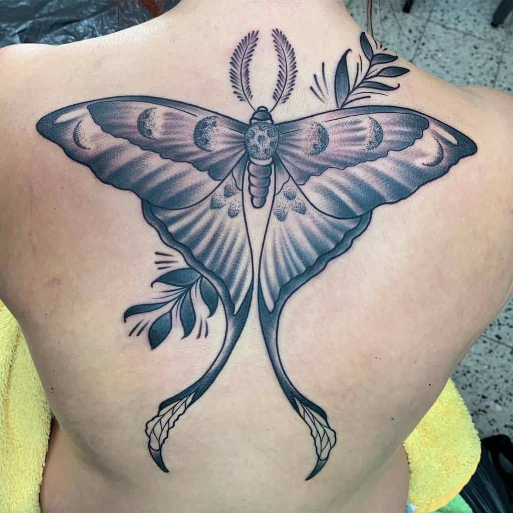A black and grey tattoo of a Luna Moth, adorned with crescent moons and botanical elements