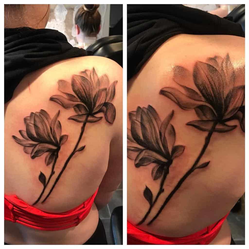 A black and gray floral tattoo featuring two delicate magnolia blooms adorns a woman's back