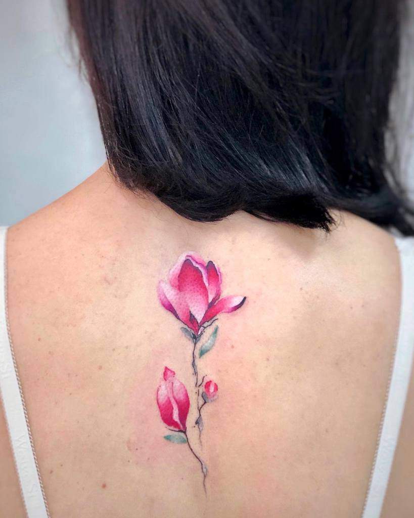 Back tattoo of delicate pink magnolias adorned with vibrant green leaves