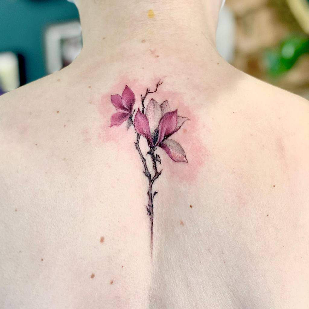A stunning floral back tattoo featuring delicate pink magnolia flowers complemented by subtle shading