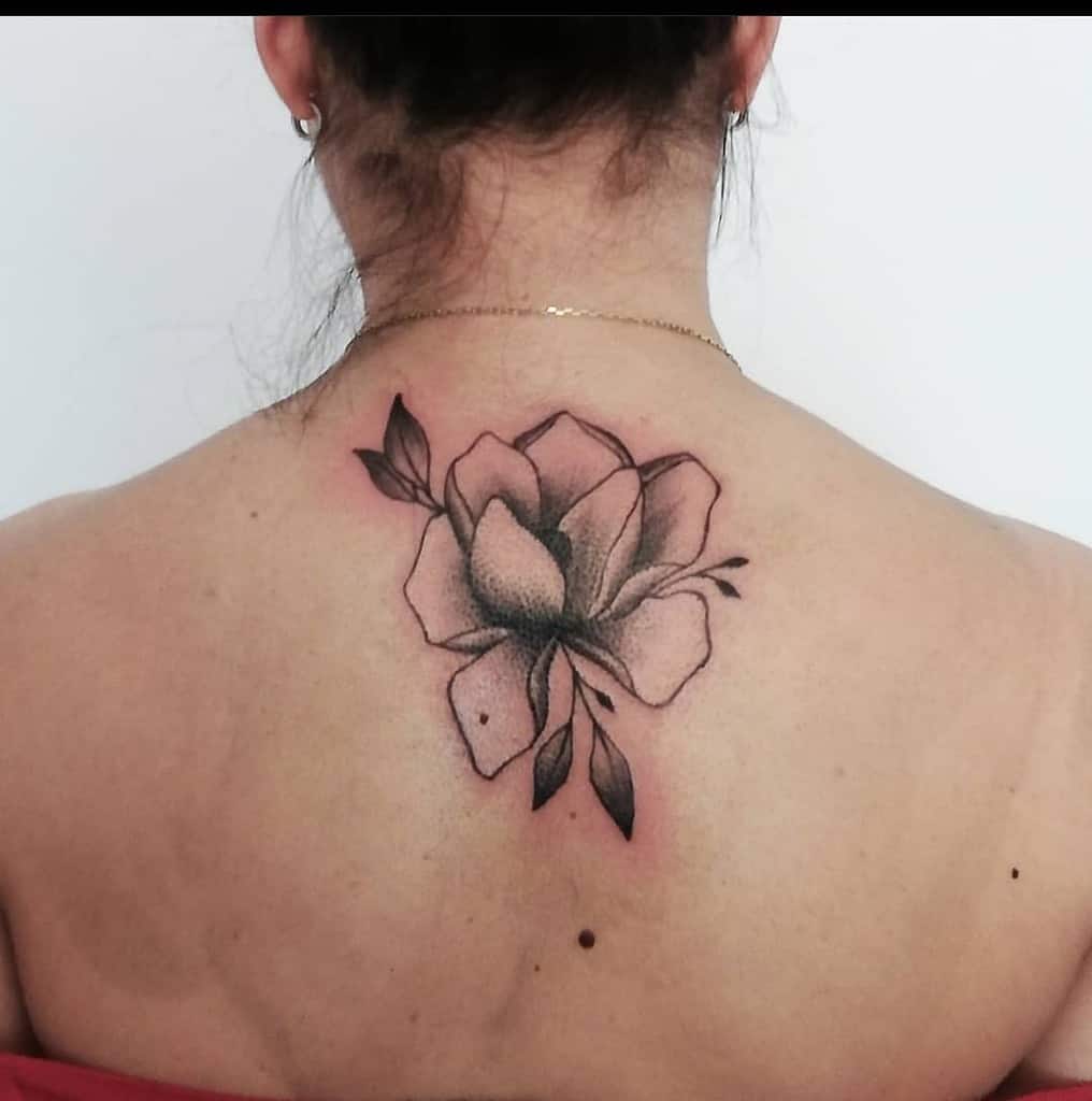 A stunning black and gray magnolia flower tattoo gracefully adorns the woman's back