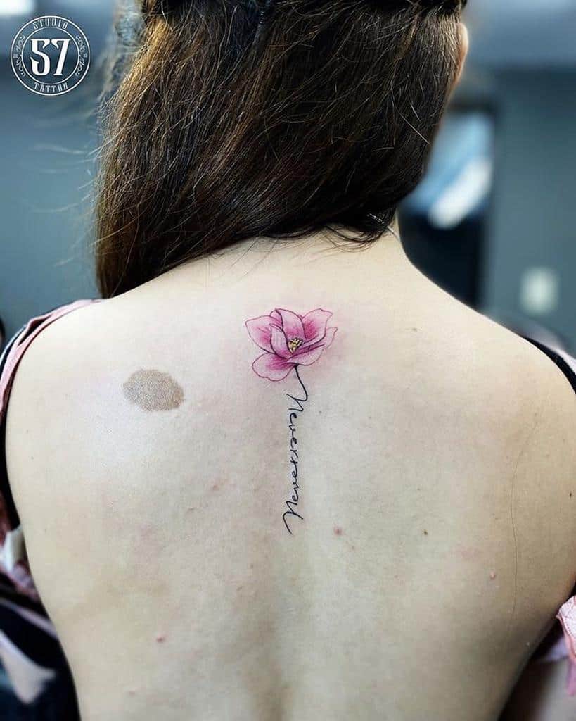 A back tattoo featuring a delicate pink magnolia blossom with elegant script nestled beneath