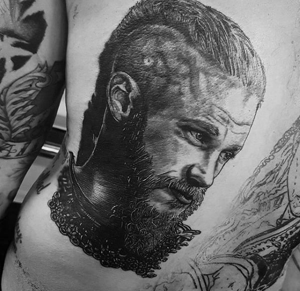 Detailed Ragnar Lothbrok tattoo on the ribs, featuring a realistic portrait with braided hair and beard