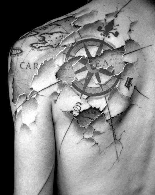Black and white shoulder tattoo of a compass and map with a torn skin illusion