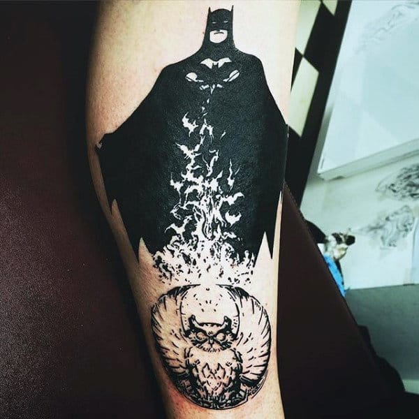 Black ink tattoo featuring a silhouette of Batman emerging from flames, blending into a detailed owl design below
