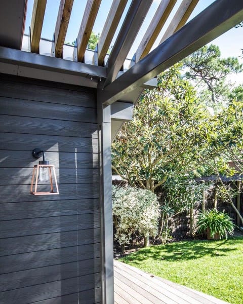 Minimal pergola with wood and metal design, outdoor lantern, and a lush backyard view.