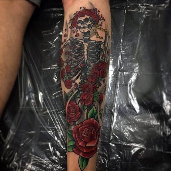 Grateful Dead forearm tattoo of a skeleton with a crown of roses, surrounded by deep red blooming roses and falling petals.