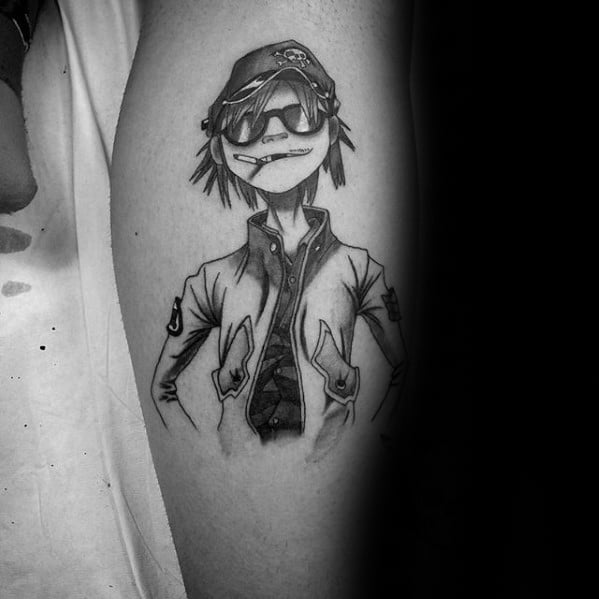Black and grey tattoo of Noodle from Gorillaz wearing a cap, sunglasses, and jacket, standing confidently with hands in pockets.