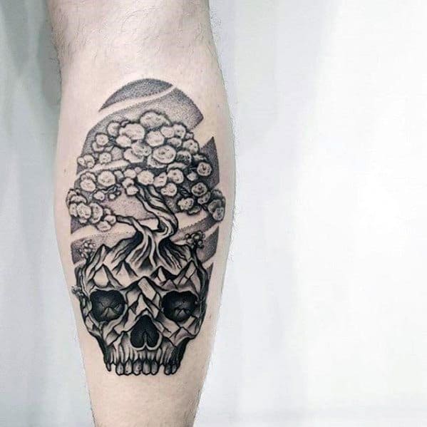 Black and grey tattoo of a tree growing from a detailed skull, with bold shading and geometric elements, symbolizing life, death, and transformation.