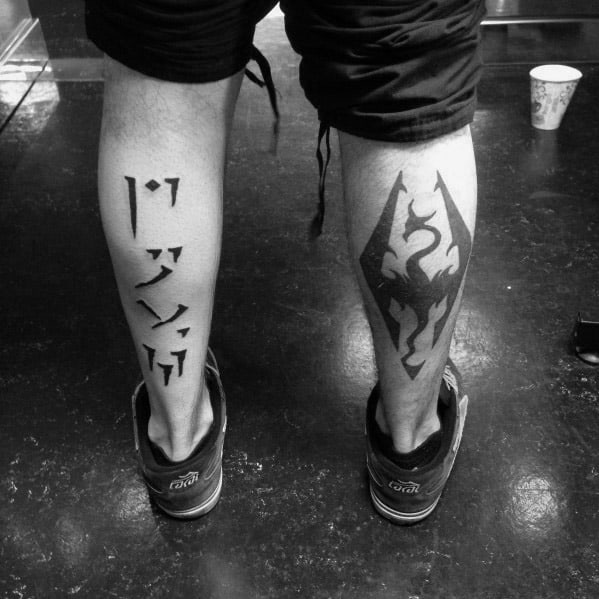 Person's tattooed legs, Skyrim text on left, dragon emblem on right leg