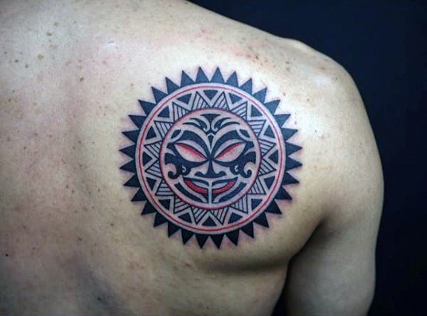 Geometric sun tattoo featuring a tribal face design on a shoulder against a dark background