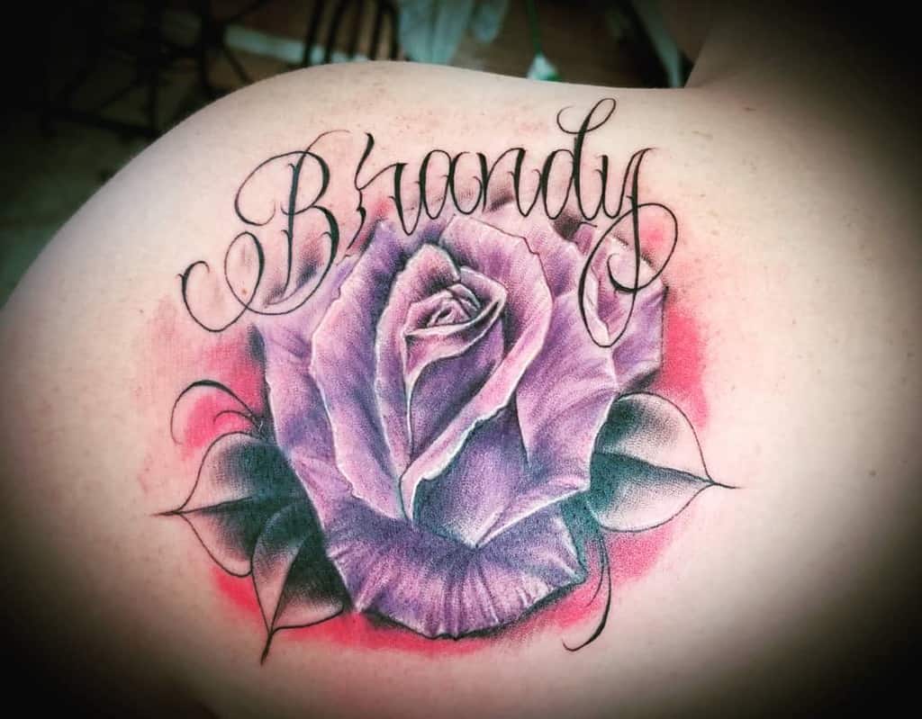 A stunning tattoo of a purple rose graces the shoulder, elegantly intertwined with the name "Brandy".