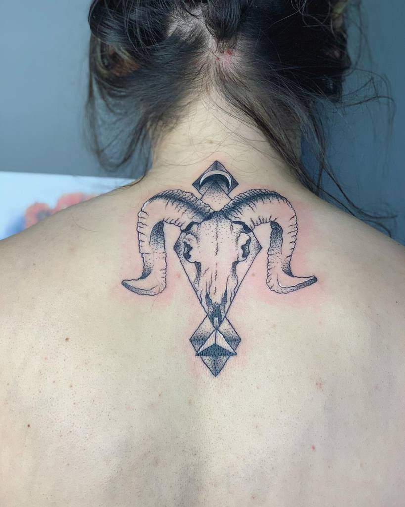 A tattoo of a ram skull with geometric shapes on the upper back