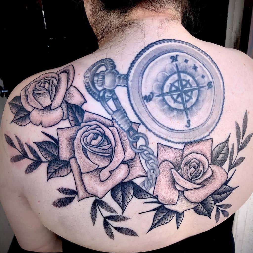 Intricate back tattoo featuring shaded roses, detailed leaves, and a vintage compass with a chain, symbolizing direction and beauty