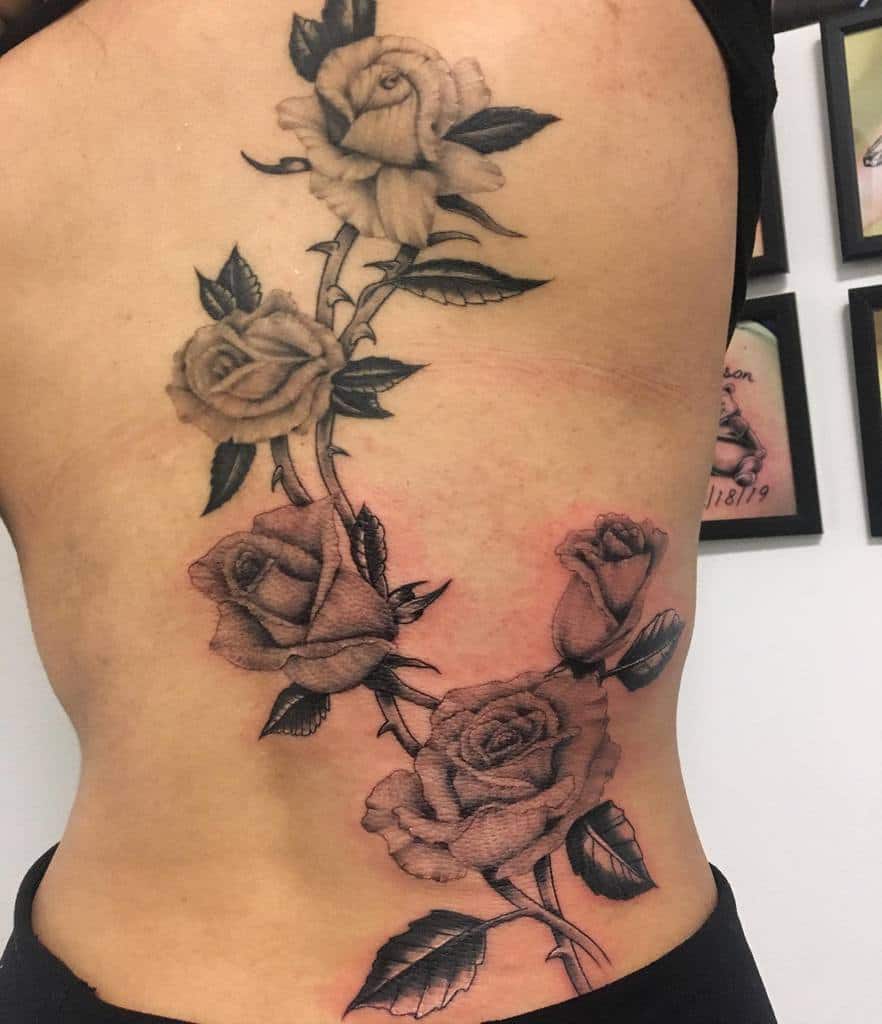 Beautiful back tattoo featuring a cascading vine of shaded roses and detailed leaves, elegantly flowing along the side