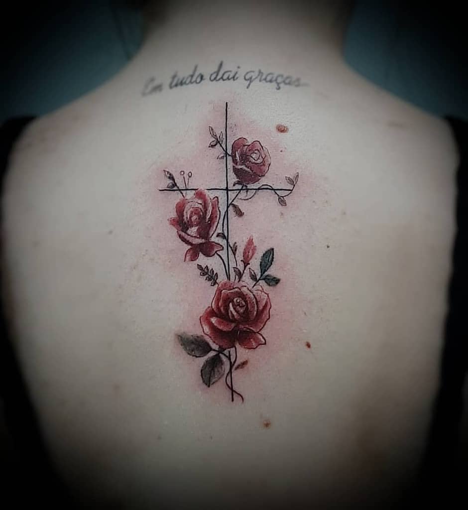 Delicate back tattoo featuring a minimalist cross intertwined with red roses and subtle vine details, accompanied by elegant script text above
