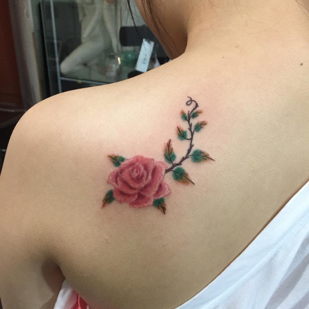 Elegant shoulder tattoo featuring a soft pink rose with delicate green leaves and a winding vine, creating a simple yet beautiful design