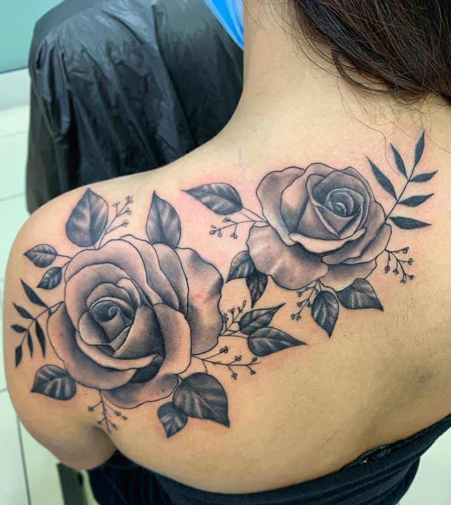 Detailed back tattoo featuring two large, shaded roses surrounded by leaves and fine botanical accents, creating a bold and elegant design