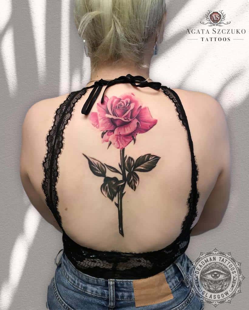 Woman with a large pink rose tattoo, complete with a delicate stem, on her back