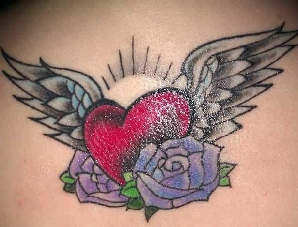 Heart with angel wings tattoo, adorned with purple roses and radiant light