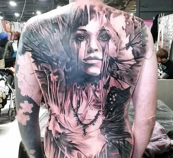 Man with a large, detailed tattoo of a woman's face and abstract designs on his back