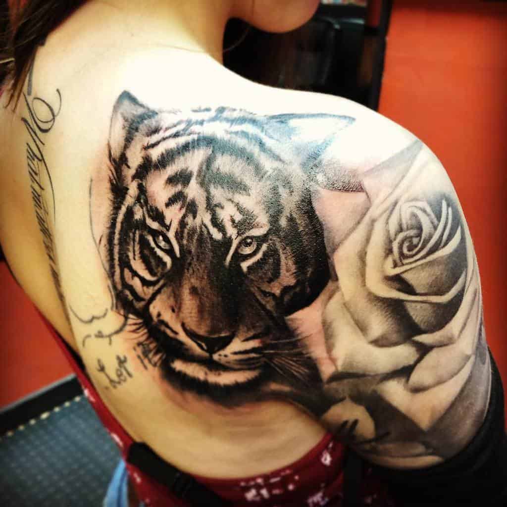 A striking tattoo of a fierce tiger intertwines with a delicate rose, gracing the shoulder and upper arm