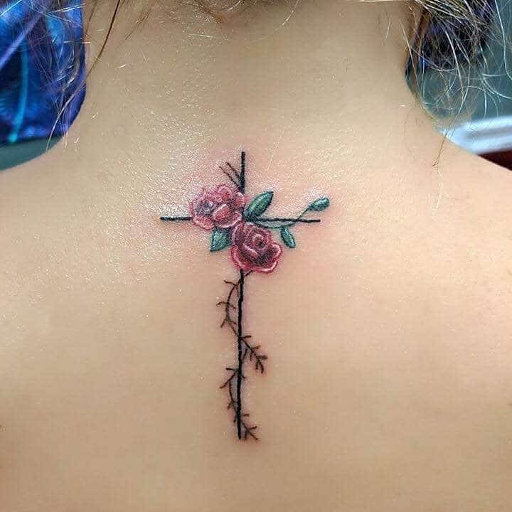 Rose and thorn cross tattoo on the upper back, featuring two pink roses, green leaves, and a black thorny stem forming a cross shape