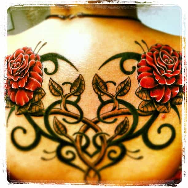 Back tattoo featuring red roses intertwined with intricate black vine designs and subtle tribal elements