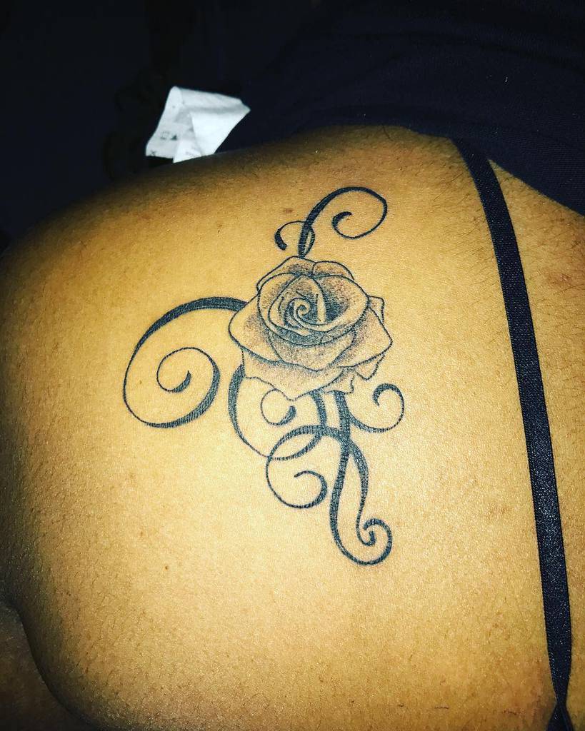 Black rose tattoo with swirling vines on a shoulder