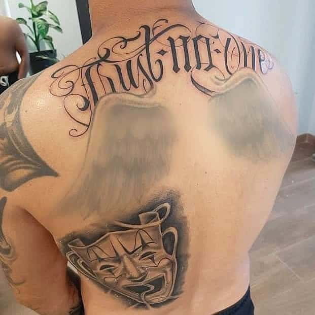Back tattoos of "Trust No One," angel wings, and theater masks