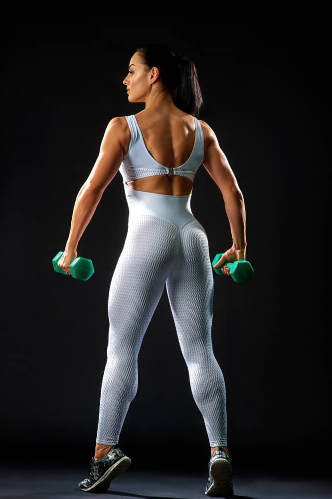 back view of muscular lady in white sportswear holding dumbbells