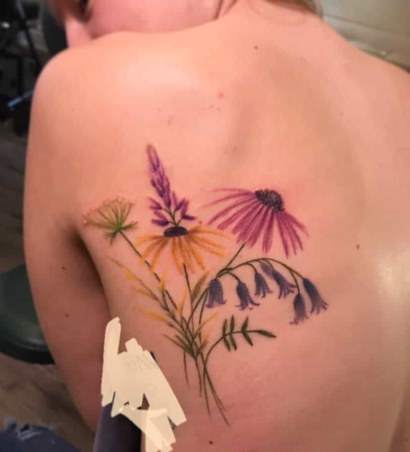 A back tattoo of colorful wildflowers, including daisies and bell-shaped blooms