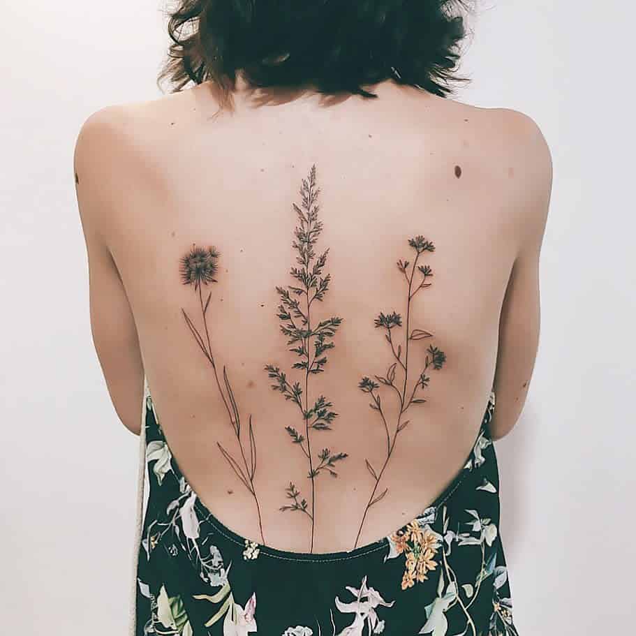 Elegant back tattoo featuring tall, minimalistic wildflowers and grasses in fine black ink for a natural, delicate look