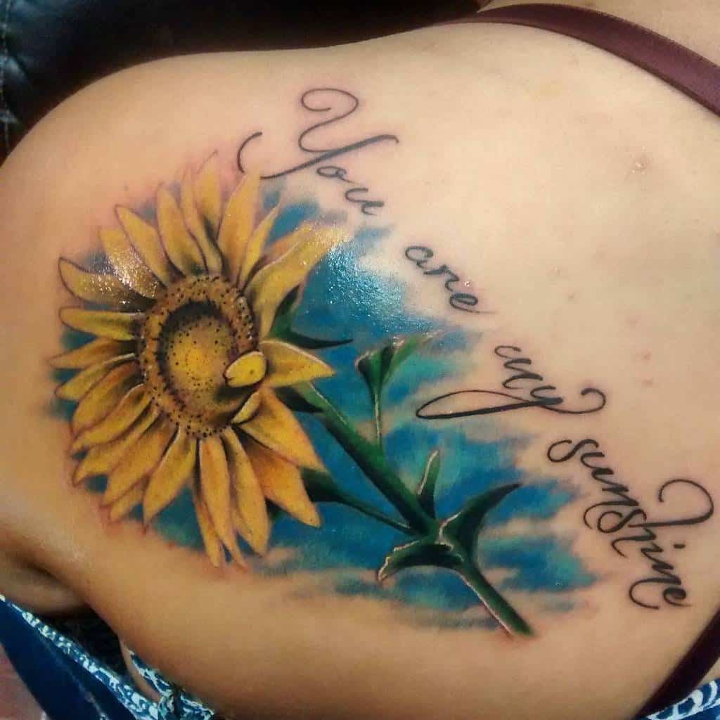 A sunflower tattoo with the text "You are my sunshine" on a shoulder