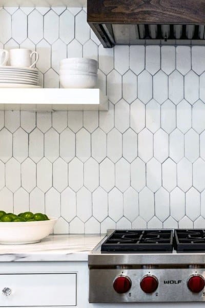 Kitchen with geometric tile backsplash, marble countertop, and stainless steel gas stovetop.