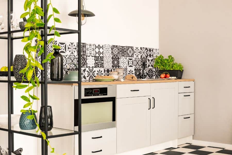 Black and white kitchen with patterned tile backsplash, wooden countertop, and potted plants.