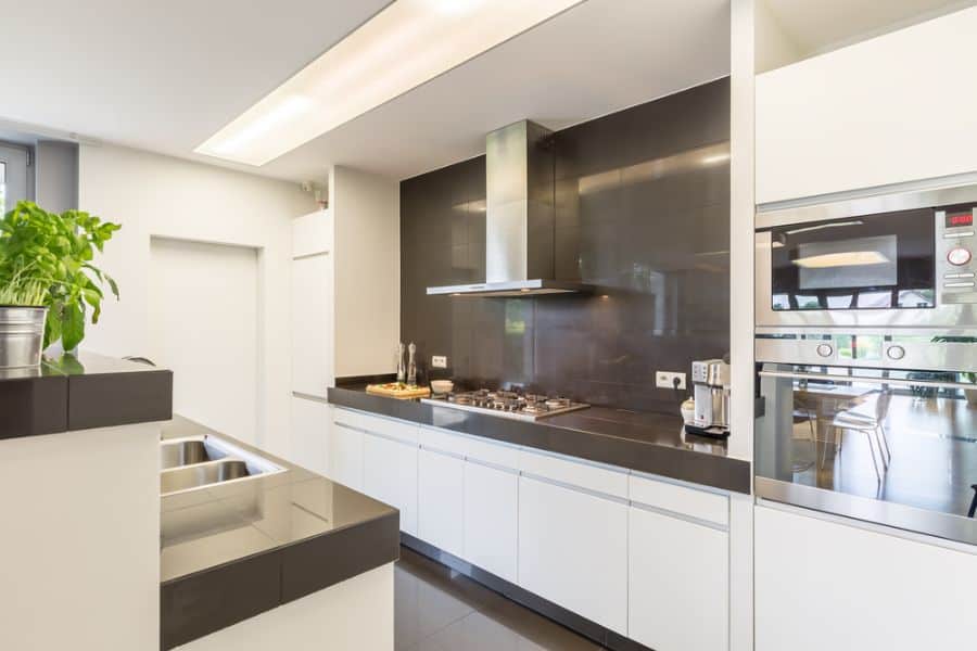 Modern kitchen with black backsplash, white cabinets, stainless steel hood, and built-in oven.