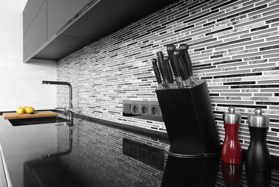 Modern kitchen with black countertop and mosaic tile backsplash.