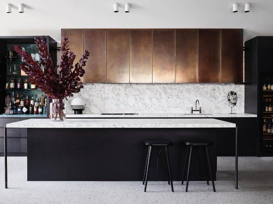 Modern kitchen with marble backsplash, black island, bronze cabinets, and bar stools.