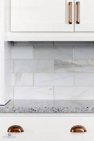 White marble subway tile backsplash with gold grout and granite countertop.