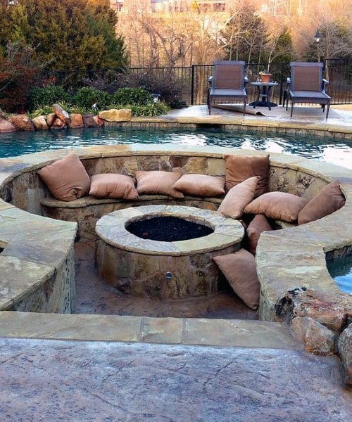 Sunken patio with cushioned seating around a fire pit, adjacent to a pool with outdoor chairs in the background