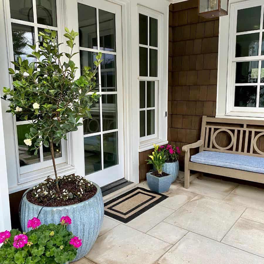 Front porch with a wooden bench, potted plants, and double glass doors featuring a small mat and flowers in blue pots