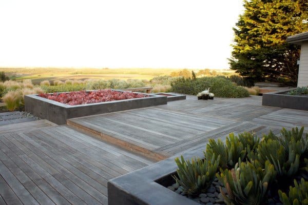 Tiered wooden deck with built-in planters featuring succulents and a view of open fields.