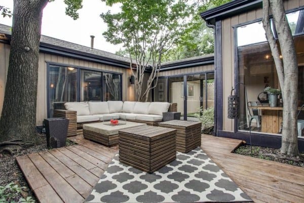 Ground-level wooden deck with cozy seating, patterned rug, and surrounding trees.
